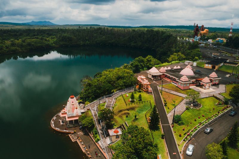Temple beside serene lake in green hills Temple complex surrounded by forest and lake