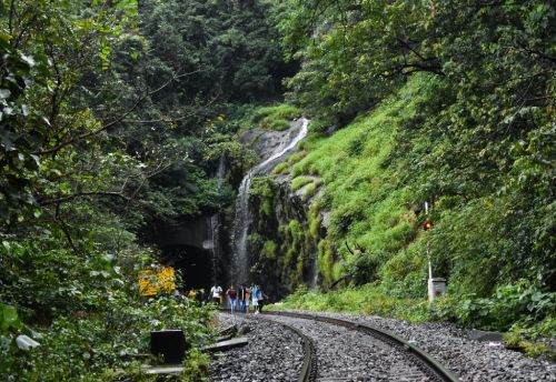 Scenic railway and forest waterfall view Waterfall flowing beside mountain railway track